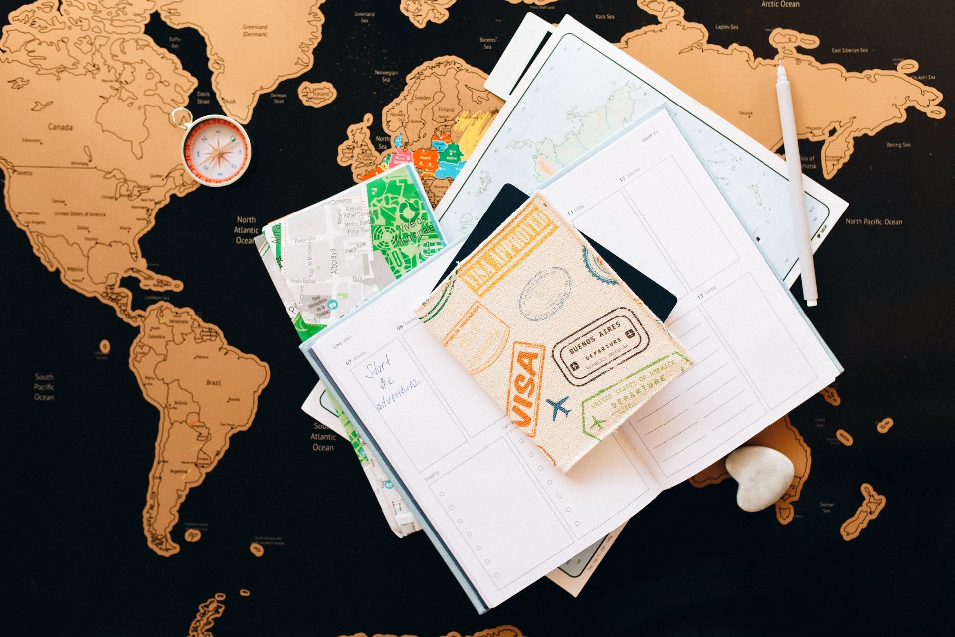 Travel planning items including map, notepad, pen, and compass on a world map background.